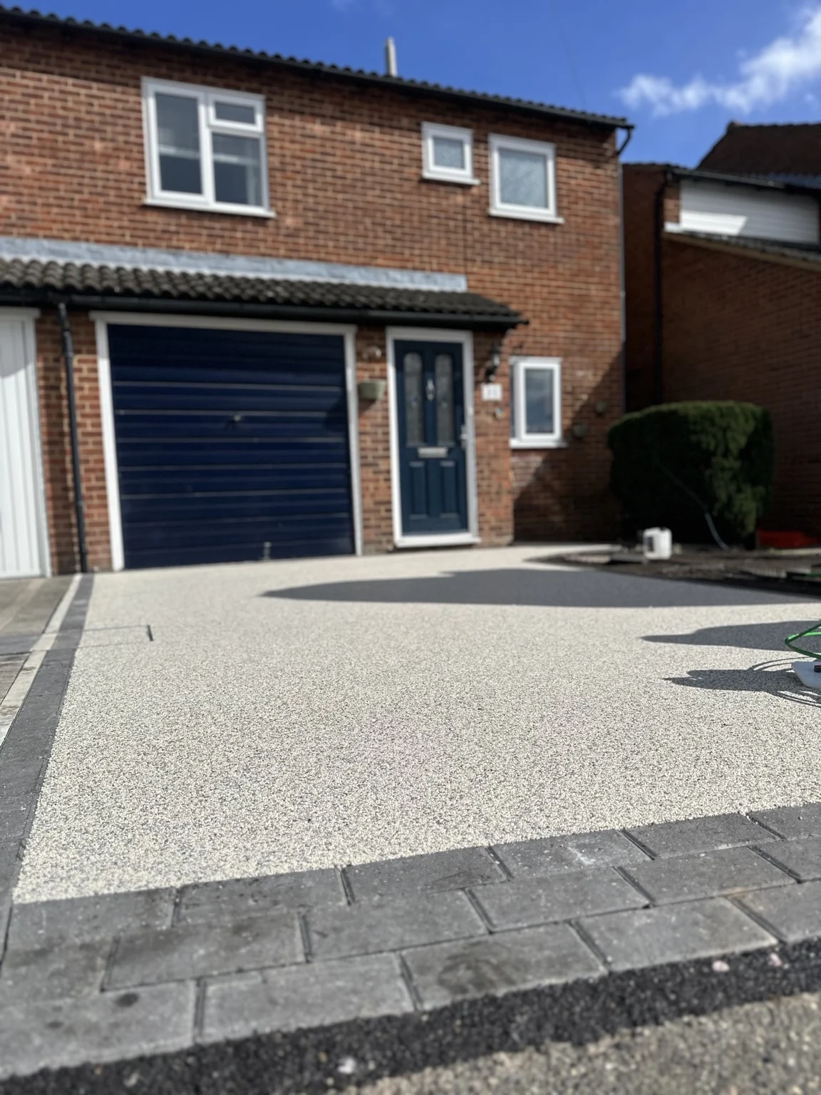Finished resin bound driveway outside a brick house with dark blue garage door